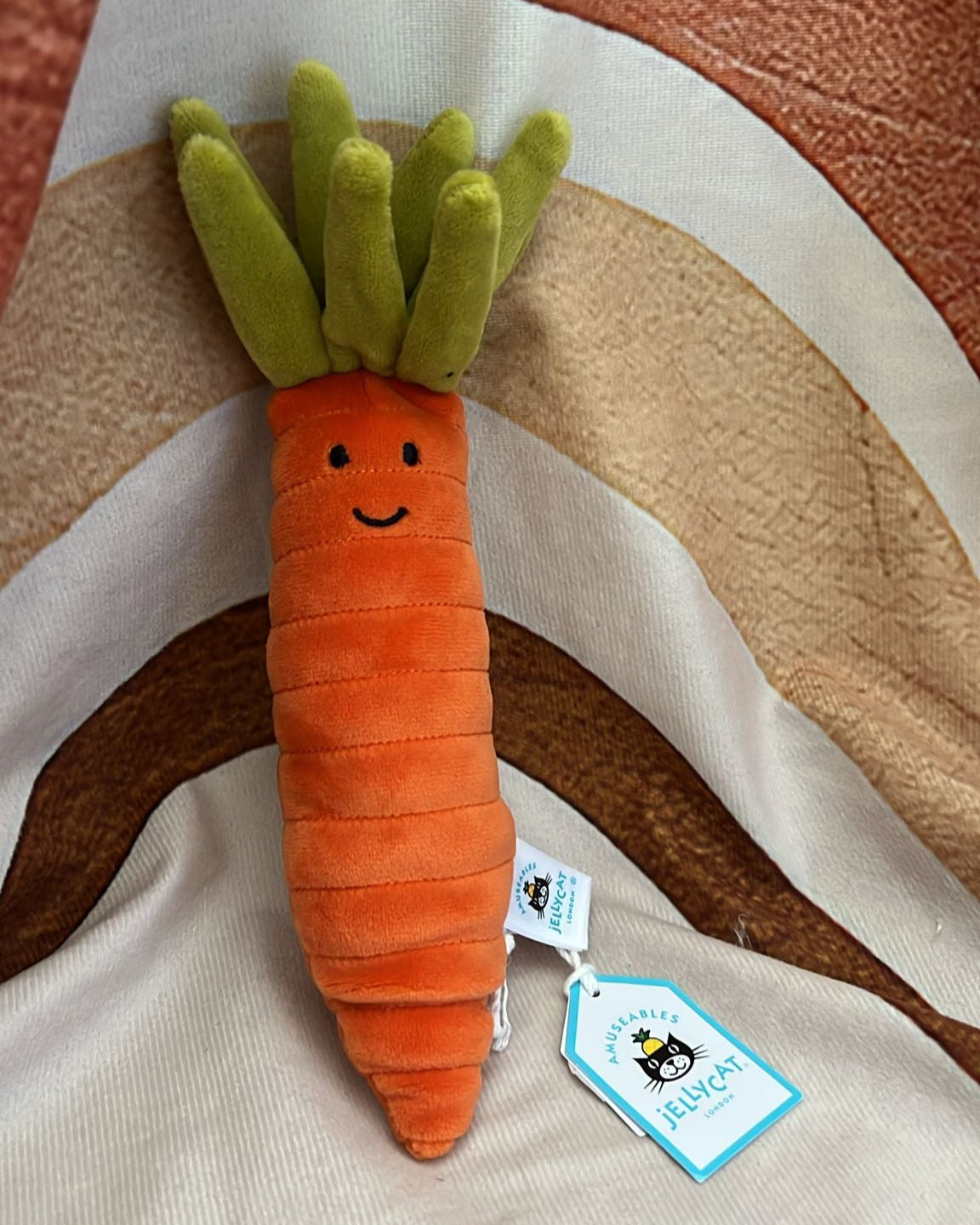 Carrot-shaped plush toy with a tag on a striped fabric background