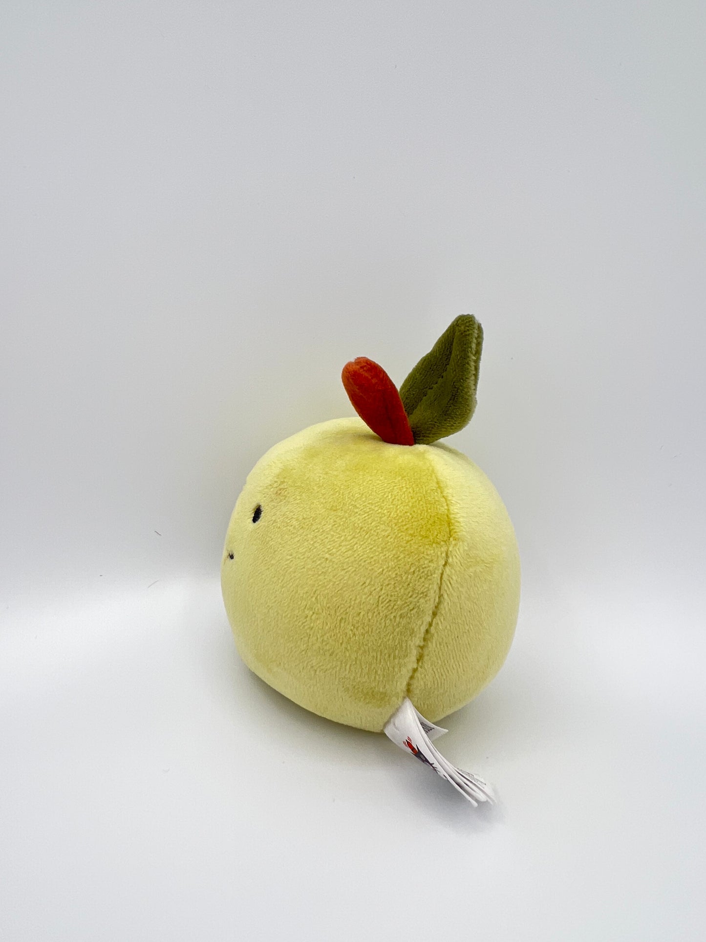 Small plush toy resembling a green apple with a red dot on a white background