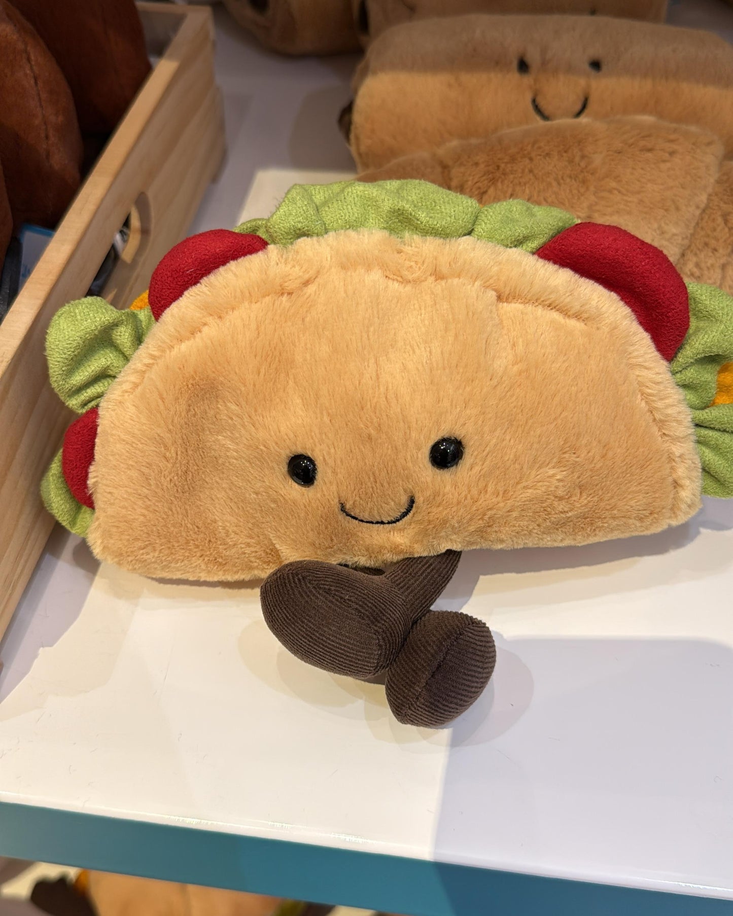 Plush toy resembling a taco with a smiling face on a shelf.