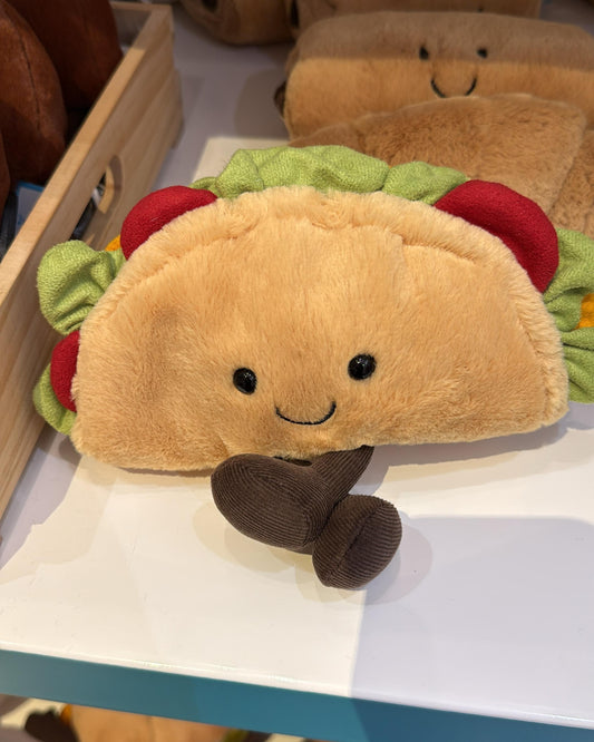Plush toy resembling a taco with a smiling face on a shelf.