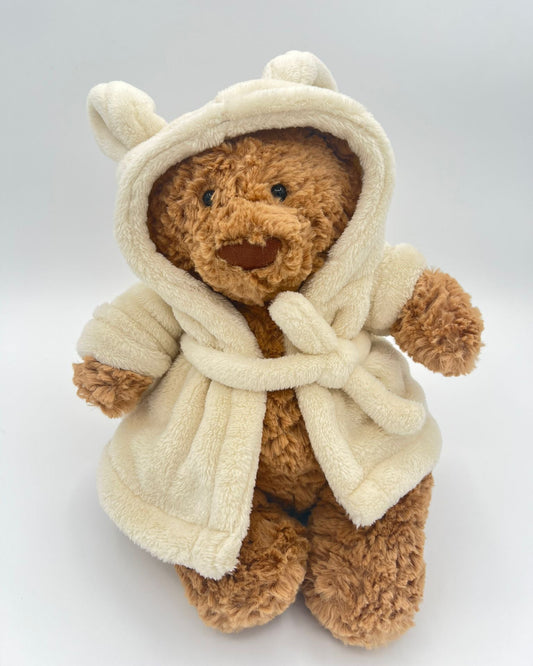 Teddy bear wearing a cream-colored robe on a light gray background