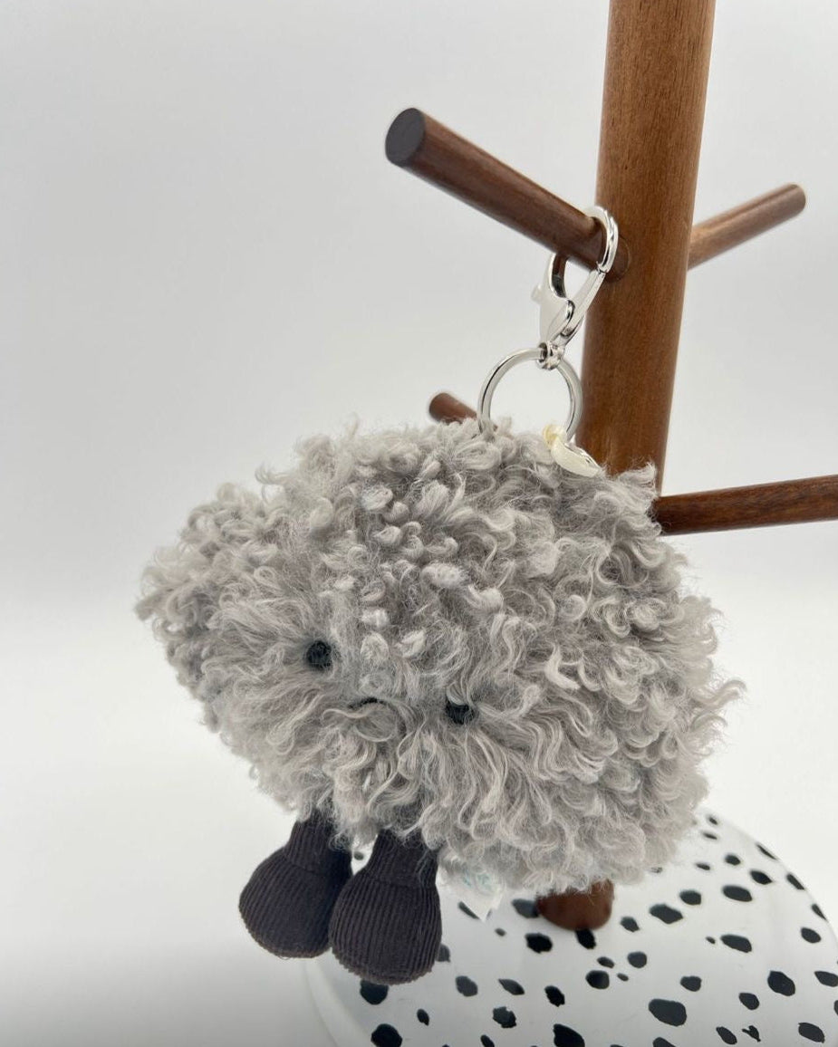 Gray fluffy keychain hanging on a wooden stand with a white background