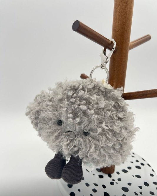 Gray fluffy keychain hanging on a wooden stand with a white background